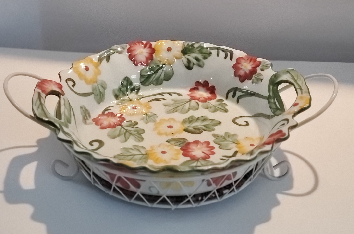Round Serving Dish With Metal Carrier 14” Round/Diameter Dish is White With Red & Yellow Flowers & Green Leaf Design Carrier is White Criss/Cross Metal withTwo (2) Handles & Removable Rattan Bottom