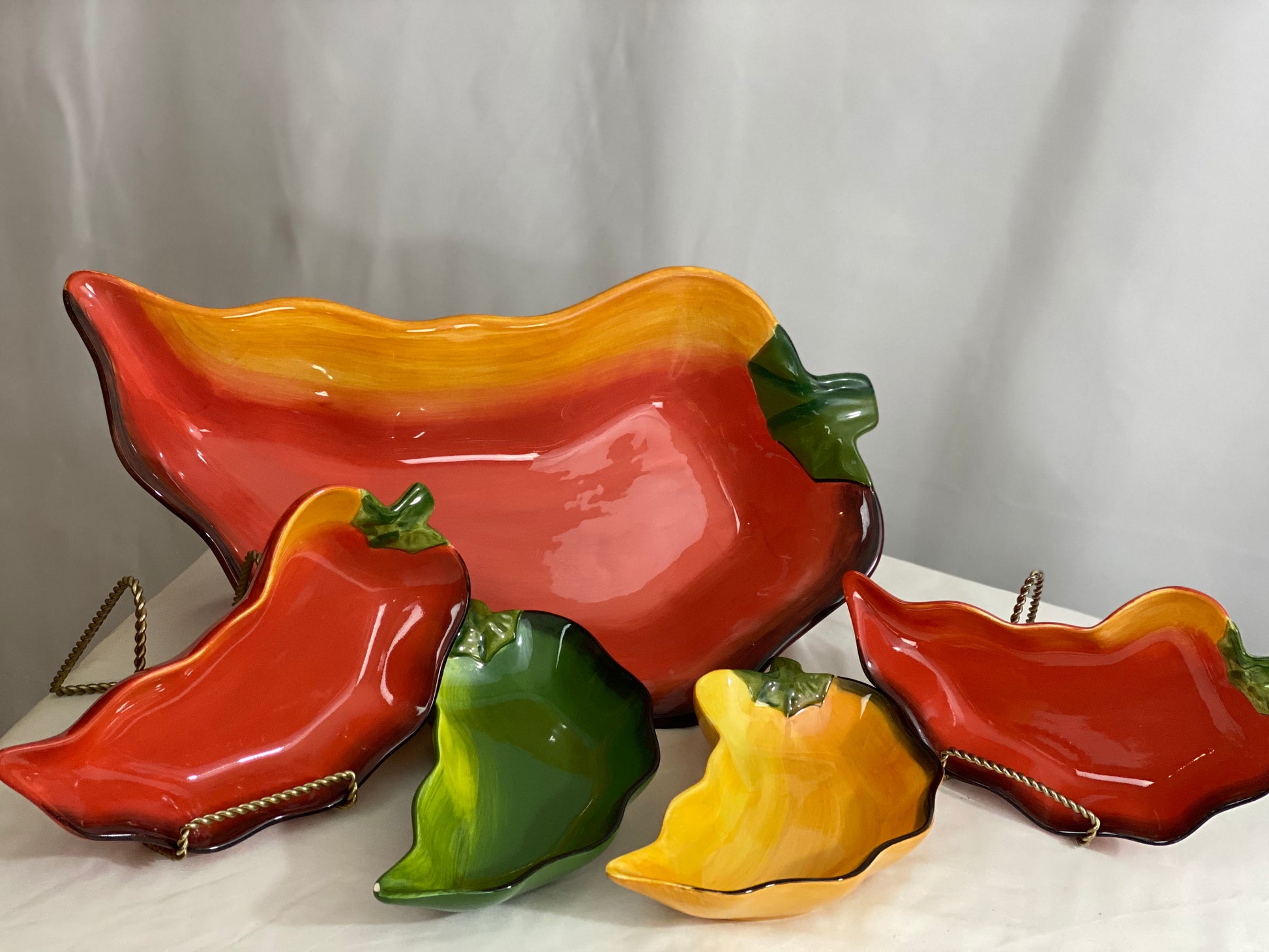 Chili Pepper Serving Set  Clay Art/Ceramic  One (1) Main Dish -- Red/Yellow  Approx 17” L x 8” W  Four Serving Dishes --  2 Red; 1 Yellow; 1 Green                                                                                                                                                                                                                                                                             Approx 9” L x 4 ½ ”W