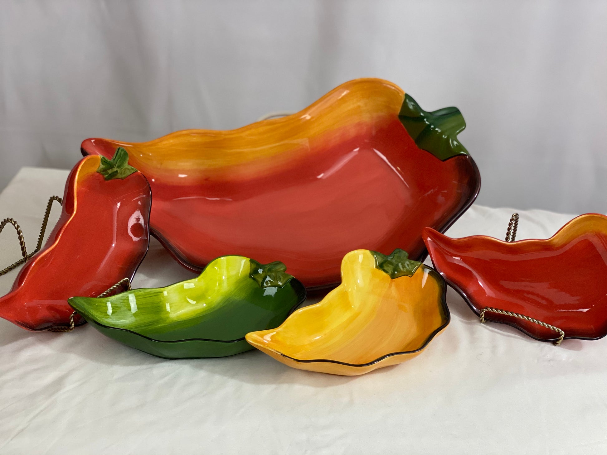 Chili Pepper Serving Set  Clay Art/Ceramic  One (1) Main Dish -- Red/Yellow  Approx 17” L x 8” W  Four Serving Dishes --  2 Red; 1 Yellow; 1 Green                                                                                                                                                                                                                                                                             Approx 9” L x 4 ½ ”W